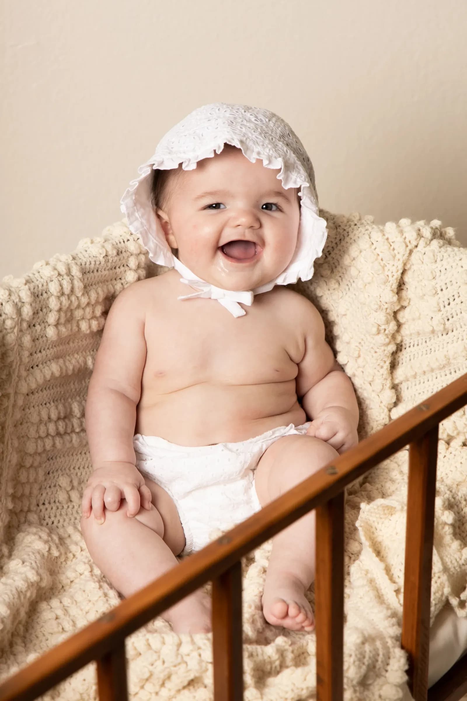 Infant in bonnet sitting on vintage crib
