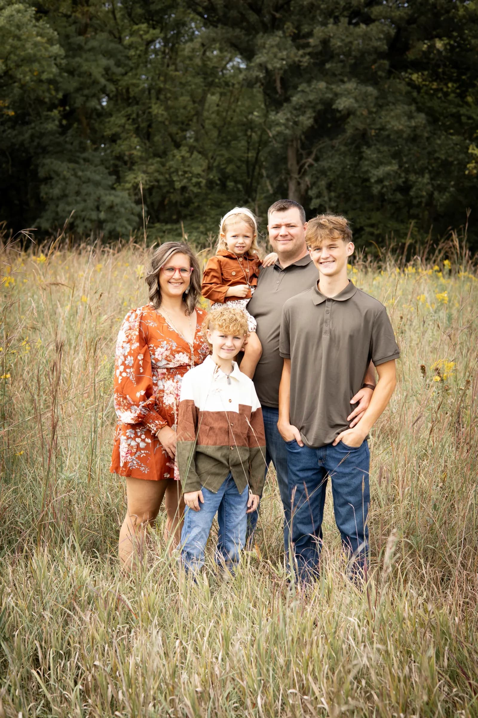 Large multigenerational family gathered around a weathered vintage green truck in a sunlit prairie field