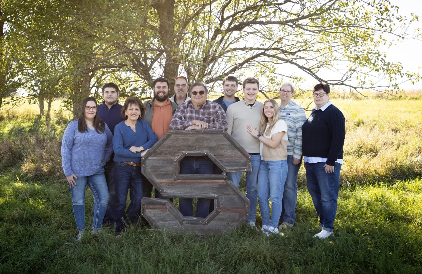 Large multigenerational family gathered a wooden letter s in a sunlit prairie field